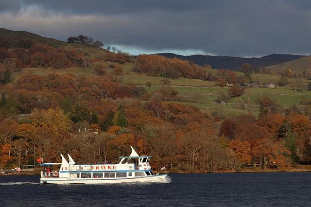 A passenger cruise boat on Windermere with autumn woodland and fells behind